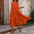 Woman wearing an orange dress with a straw bag, standing on a stone path.